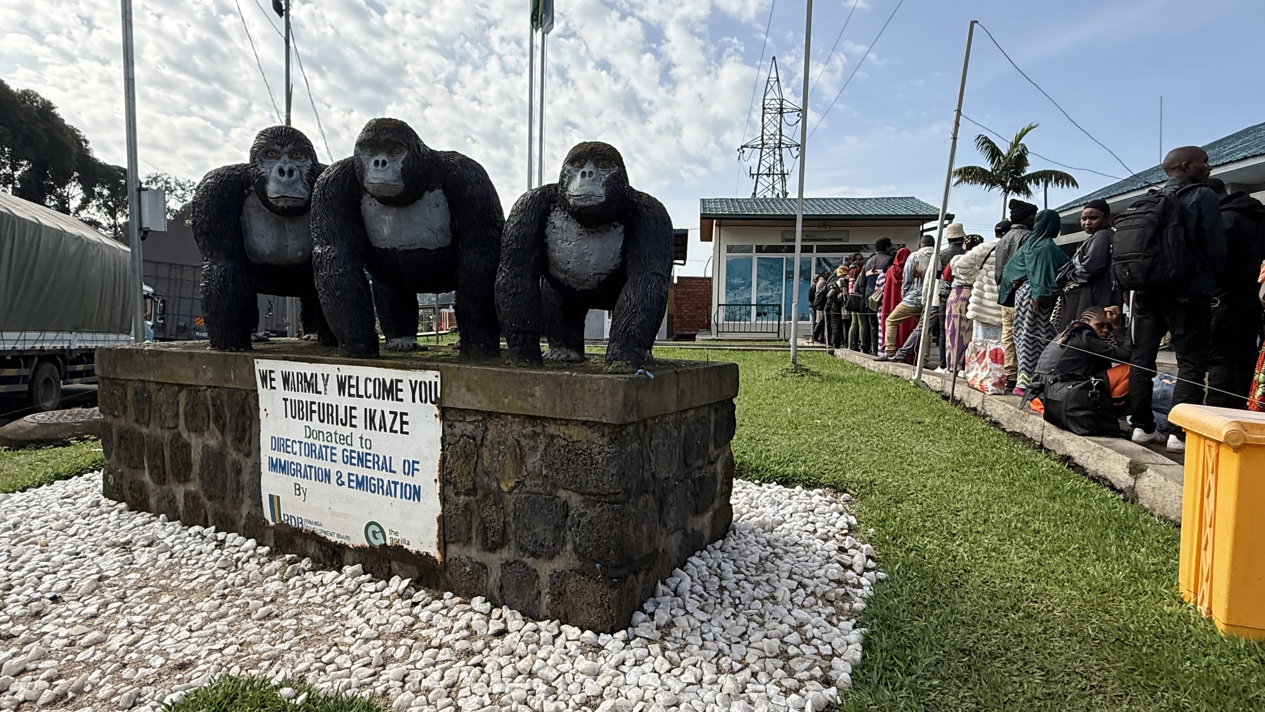 Gorilla statues at the Rwanda border crossing with immigration building and people waiting in line.