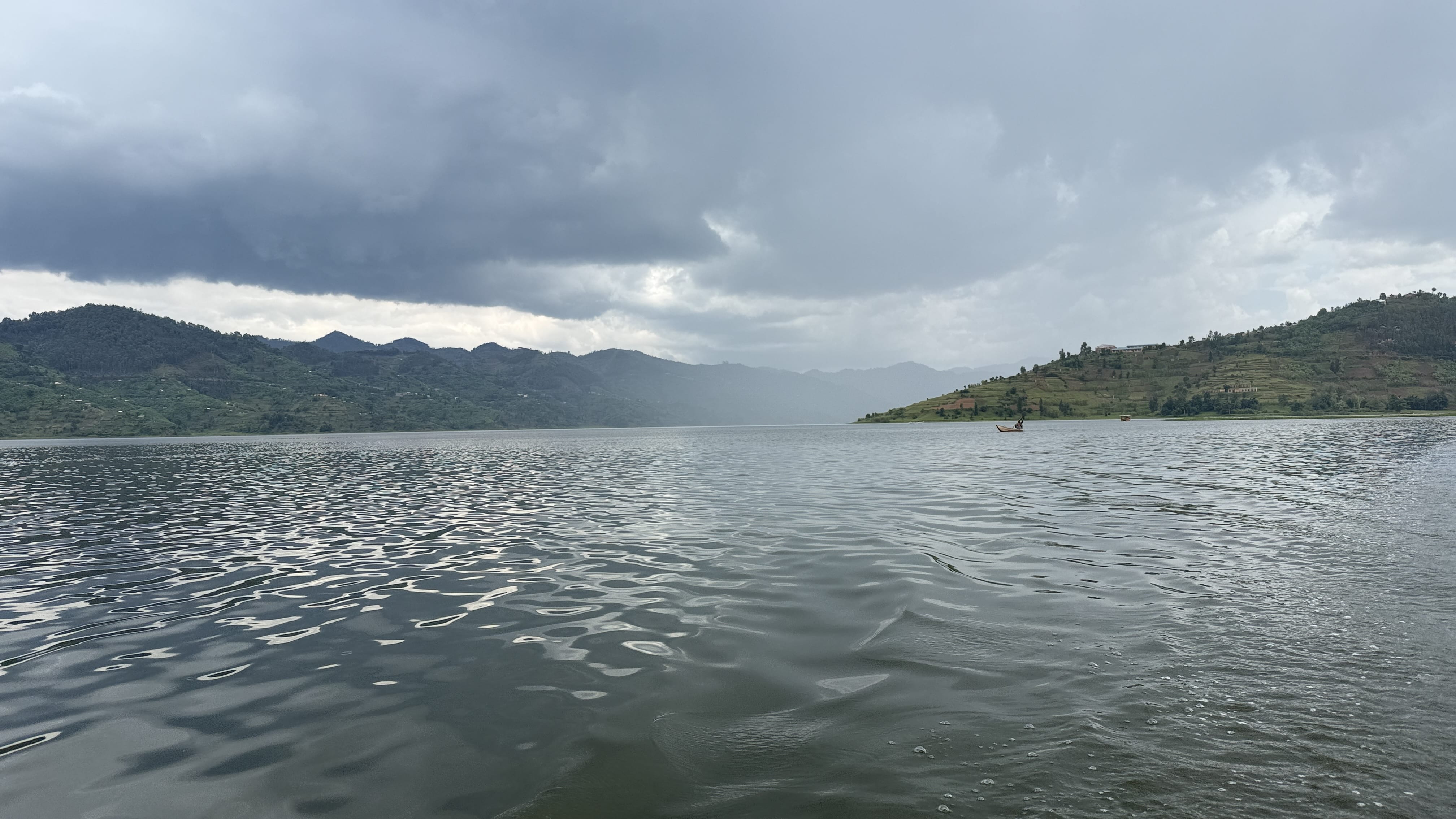 Rain clouds gathering over Lake Burera near Musanze, Rwanda, with rippling water in the foreground and green terraced hills in the distance.