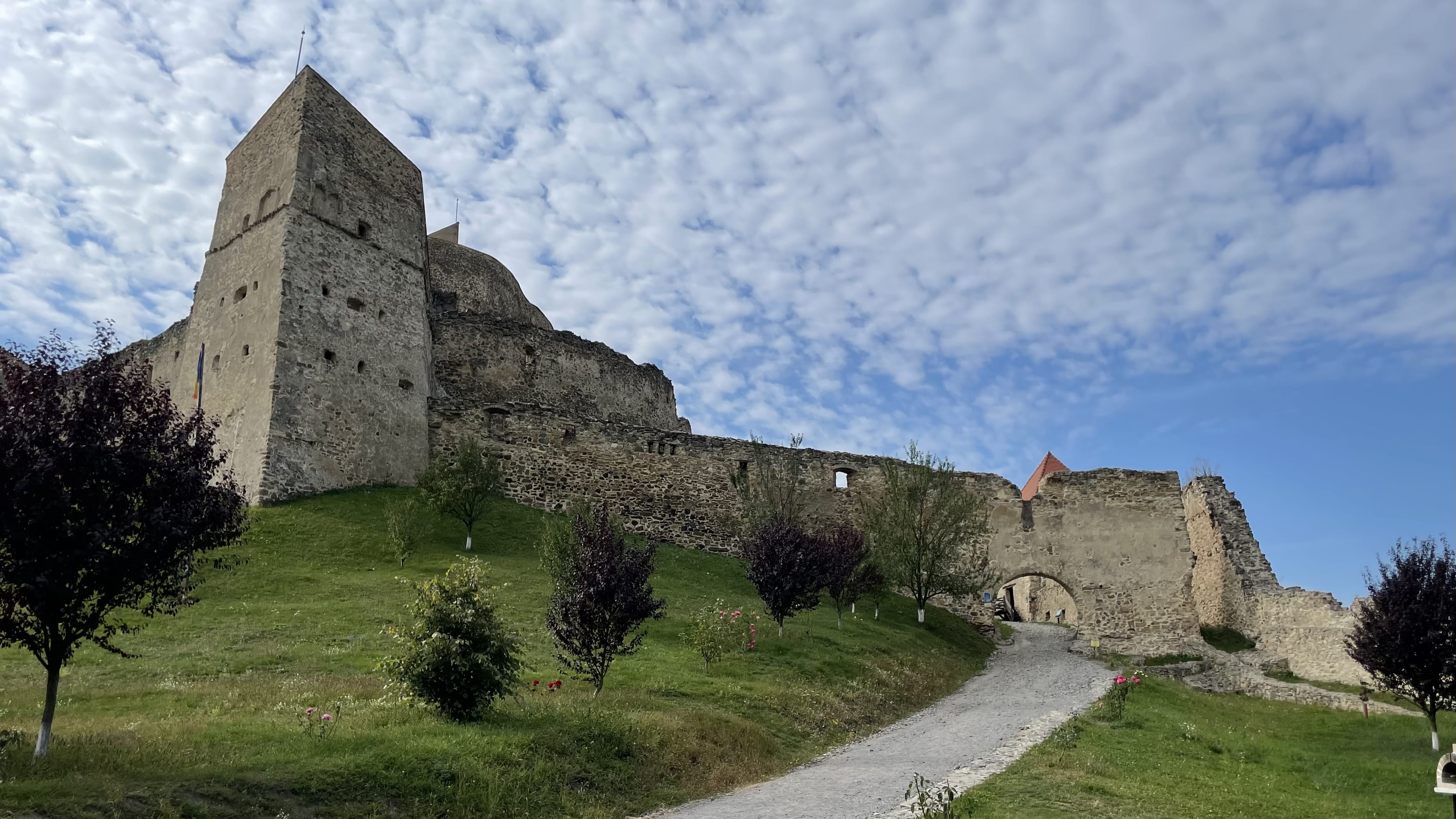 Rupea Citadel rising above green hills under a dramatic sky in Transylvania, Romania.