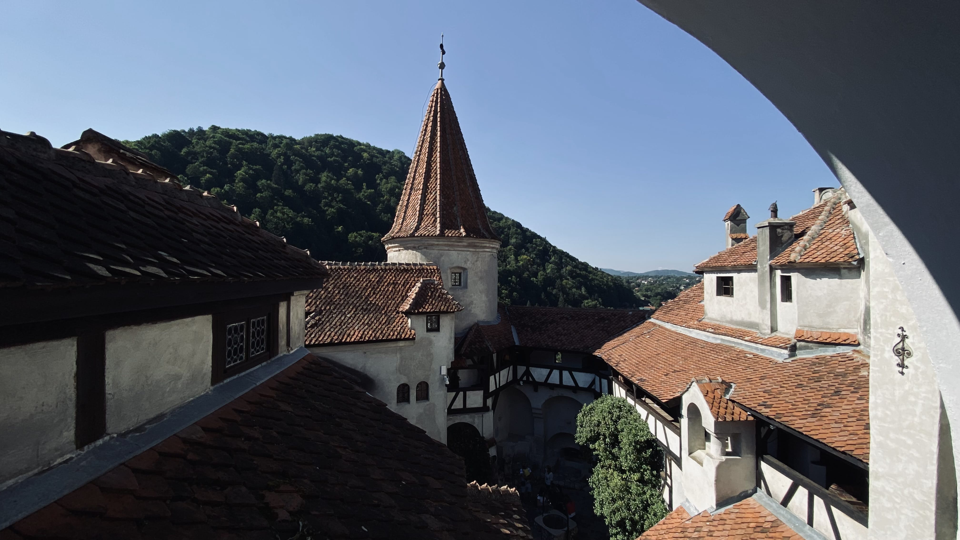 View from Bran Castle showing red-tiled rooftops, castle towers, and surrounding Transylvanian hills in Romania.