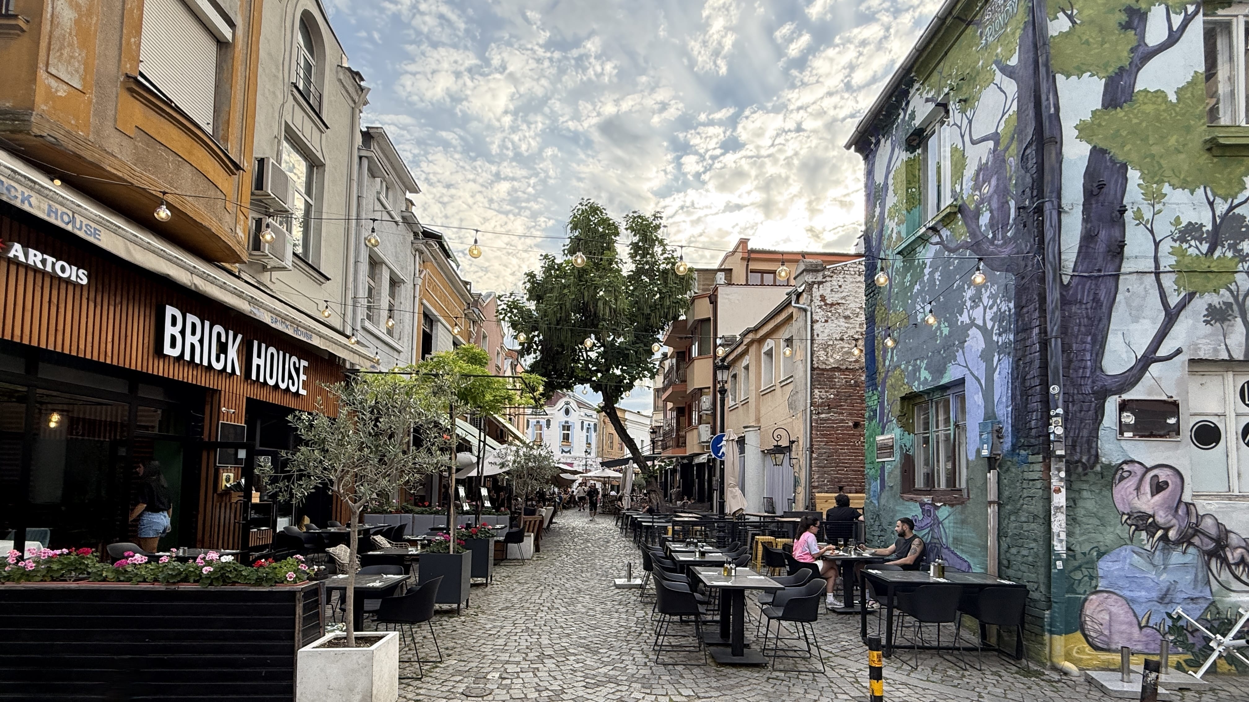 Cobblestone street with outdoor cafés and a colorful mural in Plovdiv’s Kapana Creative District